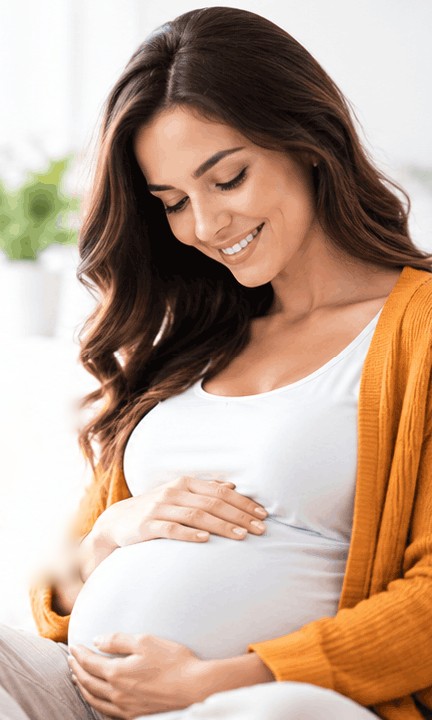 Smiling pregnant woman in an orange cardigan holding her baby bump